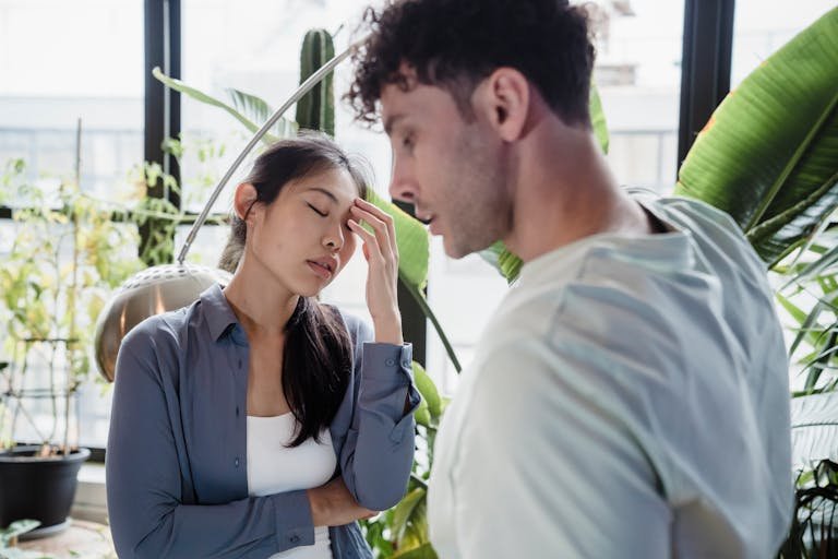 A couple experiencing a tense moment surrounded by plants in a modern space.