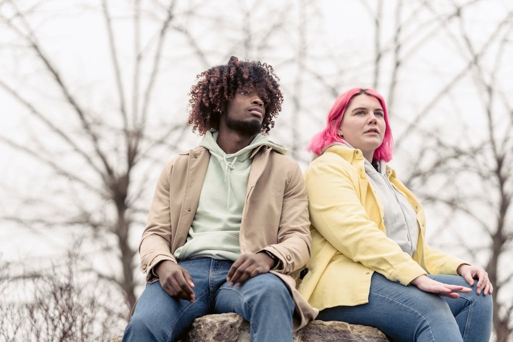 Interracial friends with unique hair colors sitting on a rock outdoors.